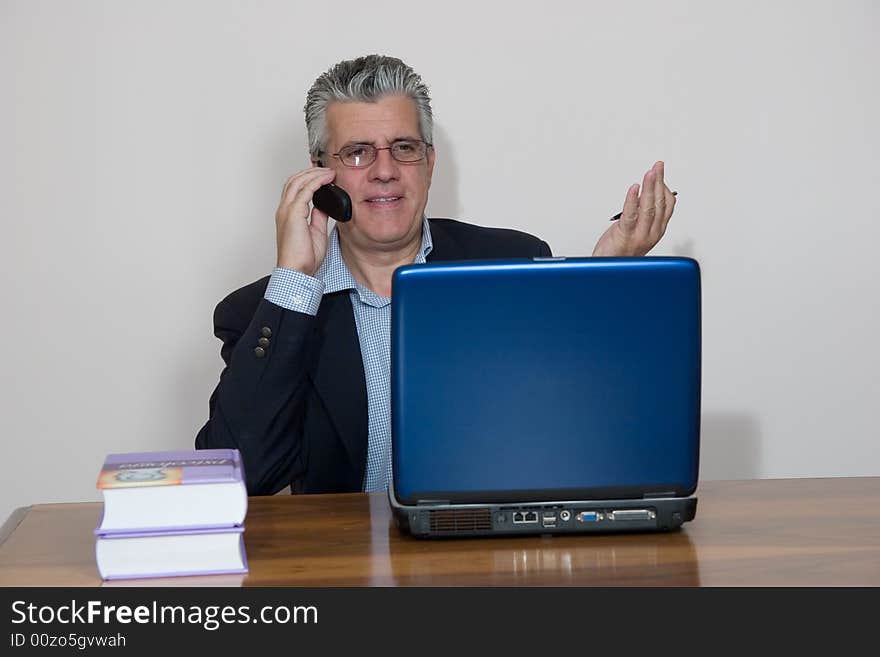 A businessman working in his study with a computer and a mobile. A businessman working in his study with a computer and a mobile