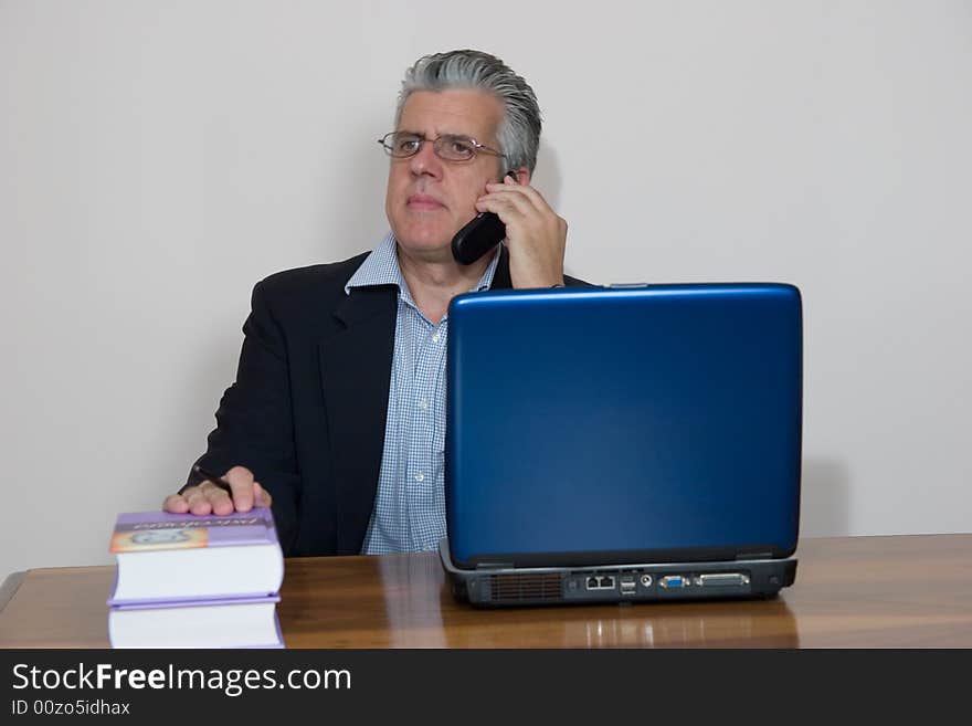 A businessman working in his study with a computer and a mobile. A businessman working in his study with a computer and a mobile