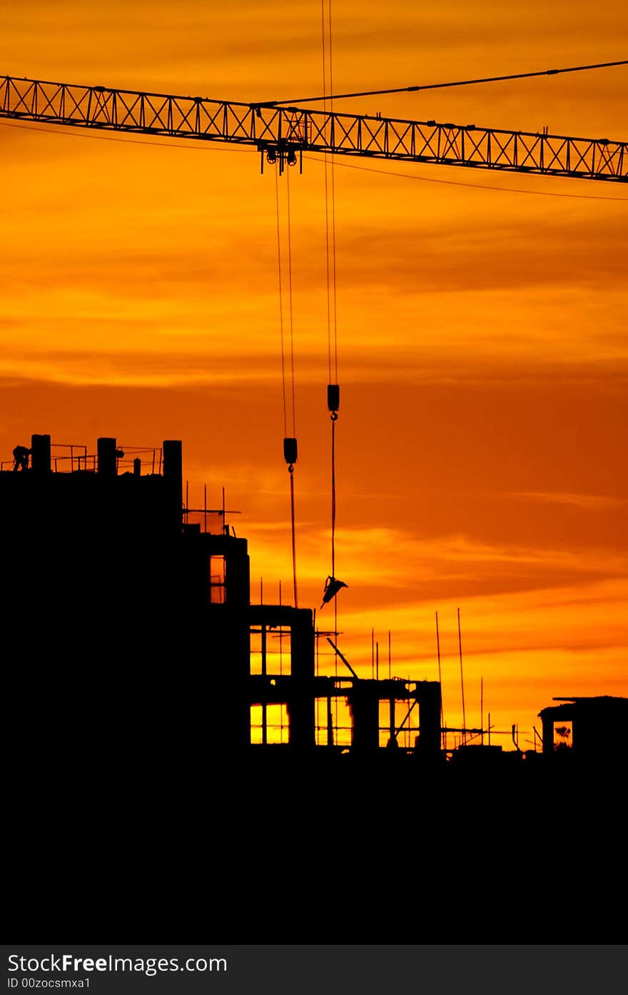 Construction of a building, cranes and other machinery as silhouettes against a background of red sunset sky. Construction of a building, cranes and other machinery as silhouettes against a background of red sunset sky