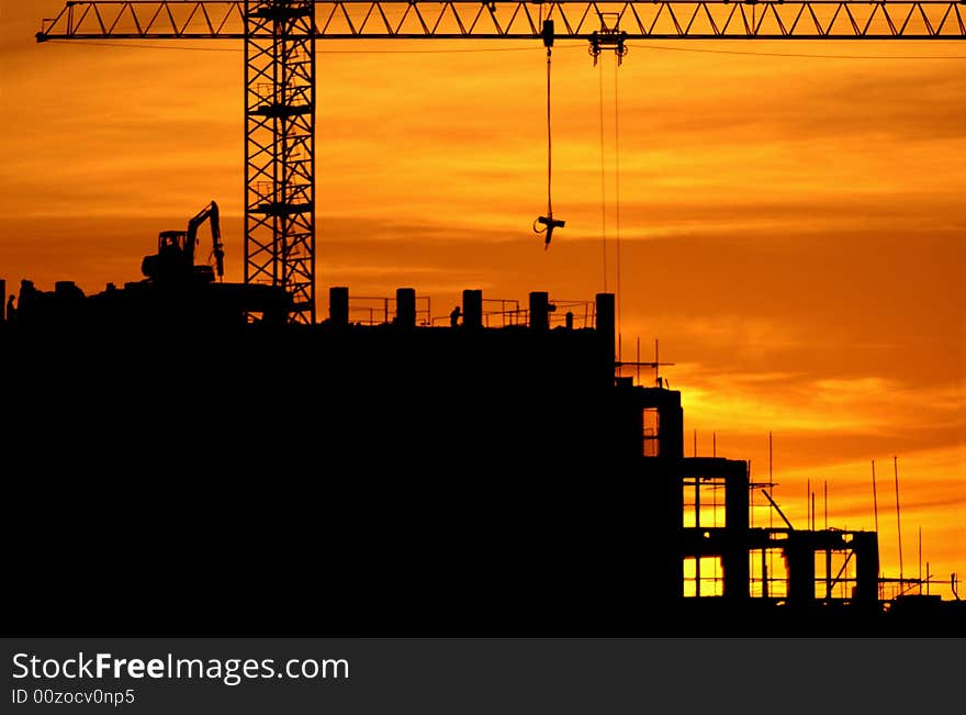 Construction of a building, cranes and other machinery as silhouettes against a background of red sunset sky. Construction of a building, cranes and other machinery as silhouettes against a background of red sunset sky