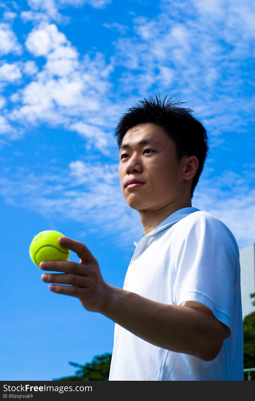 An Asian male tennis player is teeing off at the tennis court, wearing white tennis clothes. An Asian male tennis player is teeing off at the tennis court, wearing white tennis clothes.