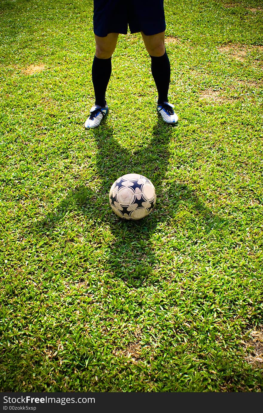 The shadow of a asian football player together with a football on green grass. The shadow of a asian football player together with a football on green grass