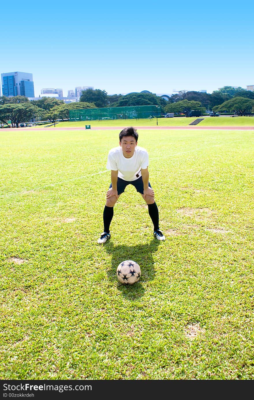 Asian Football player with football in the green court with blue sky