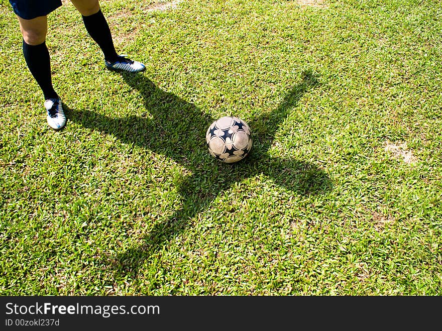 The shadow of a asian football player together with a football on green grass. The shadow of a asian football player together with a football on green grass