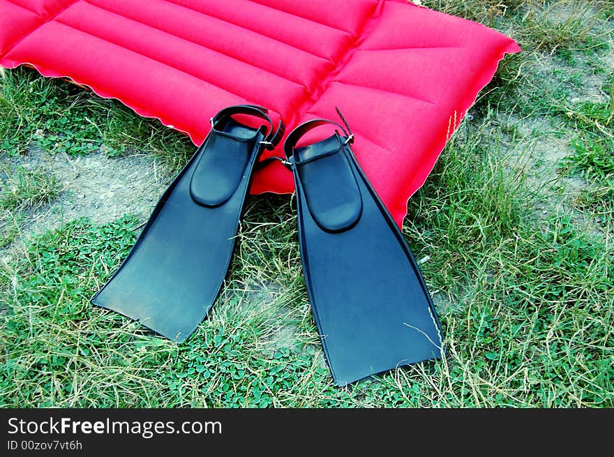 Pair of black swimfins and red mattrass on green grass. Pair of black swimfins and red mattrass on green grass