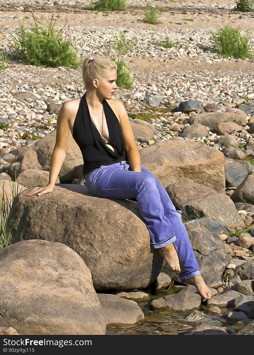 Beautiful blond girl sitting on a stone near the sea. Beautiful blond girl sitting on a stone near the sea