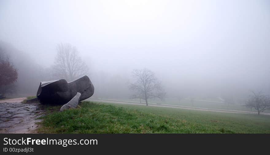 Late autumn in a park in country. Mystic fog from a morning. A thoughtful stone lies on the side of a road of road. Late autumn in a park in country. Mystic fog from a morning. A thoughtful stone lies on the side of a road of road.