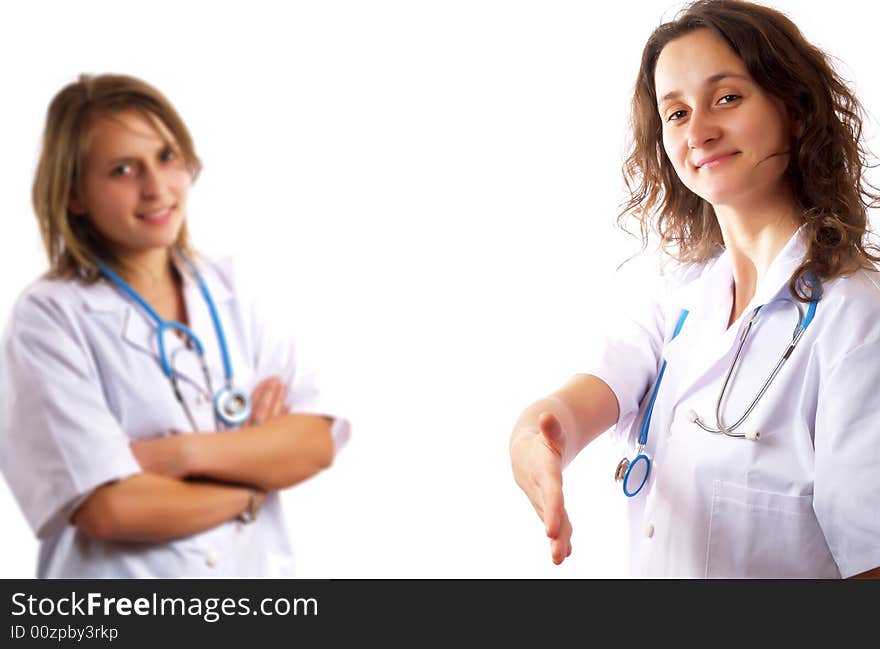 A pretty female doctor is smiling and she is holding her hand out for handshaking. Behind her there is her doctor colleague. They have stethoscopes and they are wearing white coats. A pretty female doctor is smiling and she is holding her hand out for handshaking. Behind her there is her doctor colleague. They have stethoscopes and they are wearing white coats.