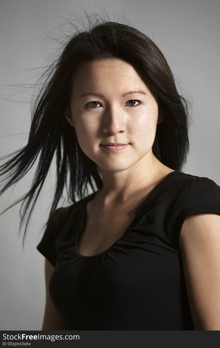 Head and shoulders portrait of young Asian woman against a gray background.