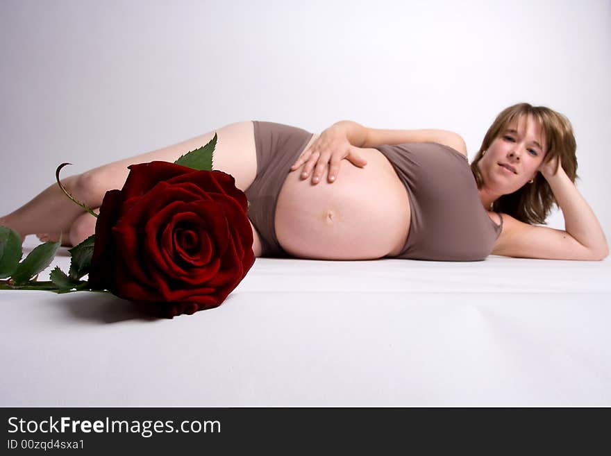 A pregnant woman lying on the floor and holding her belly with red rose in the front.