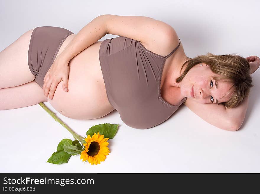 A pregnant woman lying down and looking up in to the camera. Next to her is a sun flower.