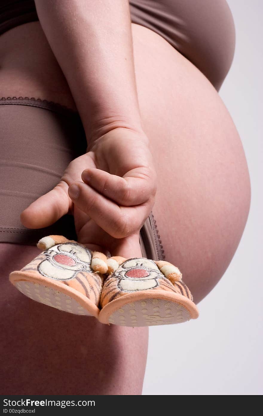 Little shoes holded in the fingers of a pregnant mother. Little shoes holded in the fingers of a pregnant mother