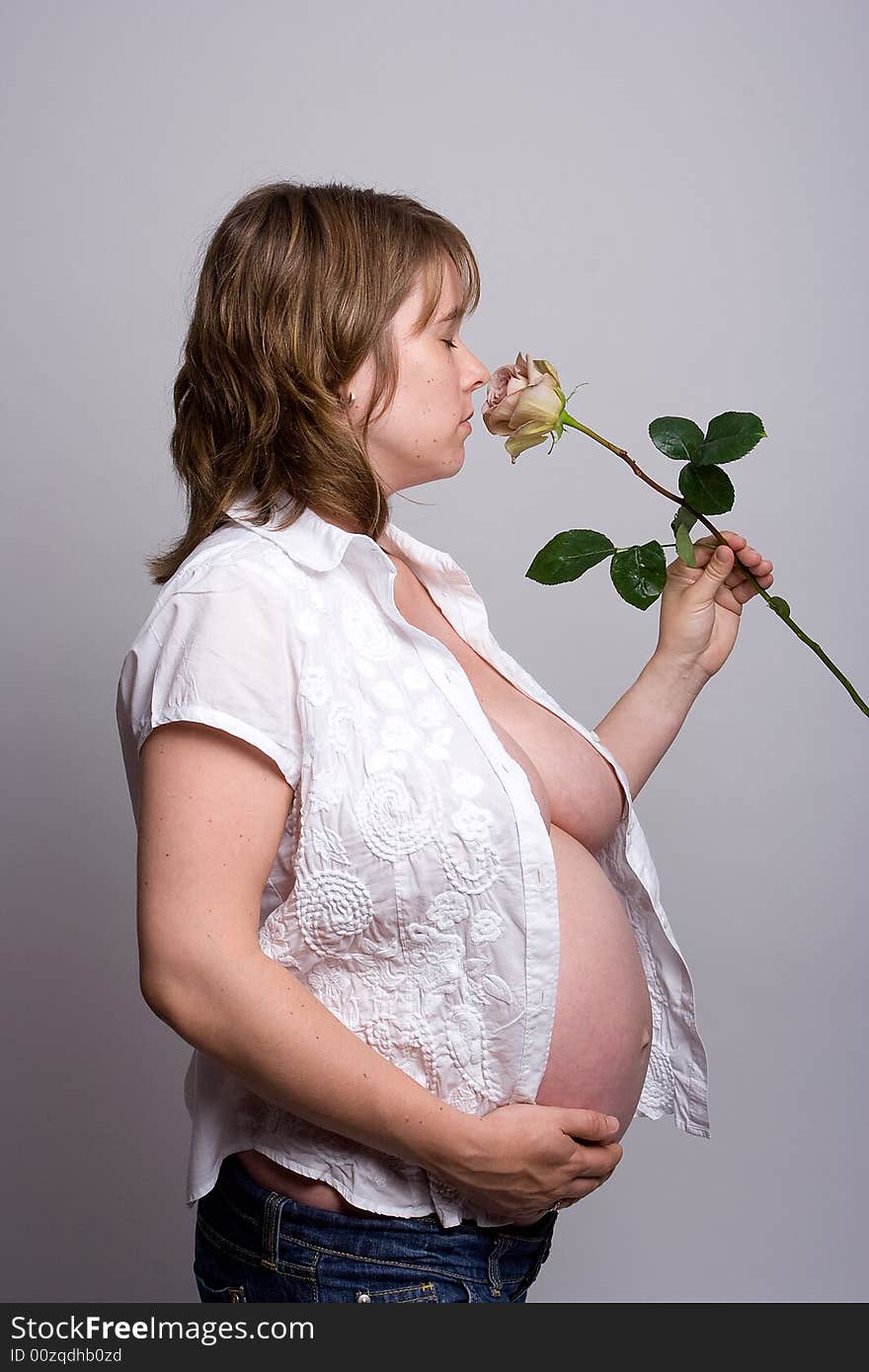 A pregnant woman holding her belly and smelling a pink rose. A pregnant woman holding her belly and smelling a pink rose