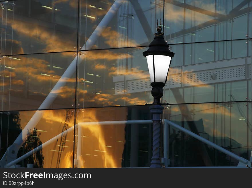 Old lantern and abctract modern glass building with sunset sky reflection