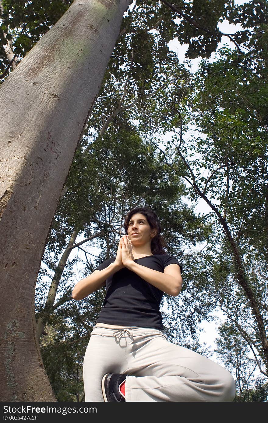 Woman In Yoga Pose Next To Tree In Park - Vertical