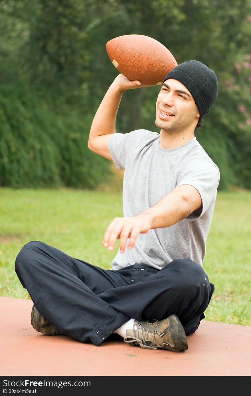 A man sitting, preparing to throwing a football, at a park, smiling. - vertically framed. A man sitting, preparing to throwing a football, at a park, smiling. - vertically framed