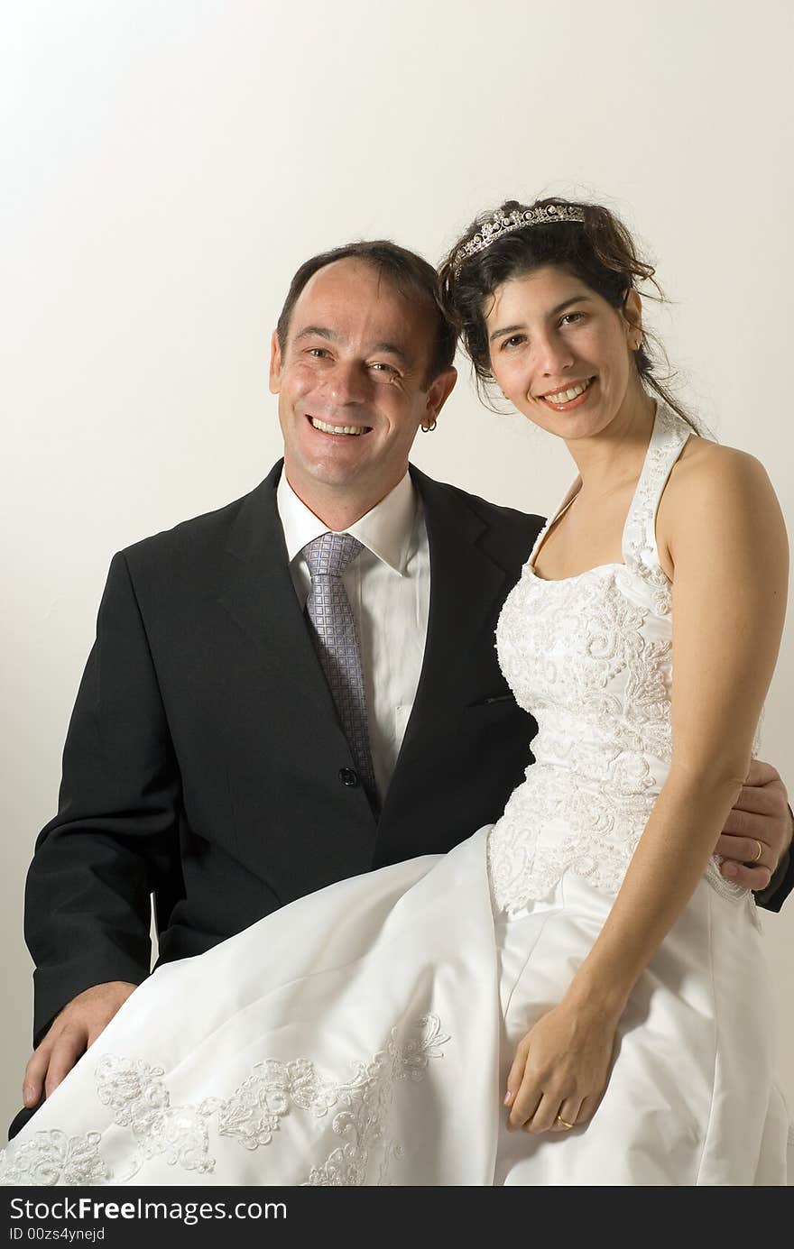 A couple of newly weds, sit on a chair, smiling for the camera. The wife sits on the husband's lap. - vertically framed. A couple of newly weds, sit on a chair, smiling for the camera. The wife sits on the husband's lap. - vertically framed