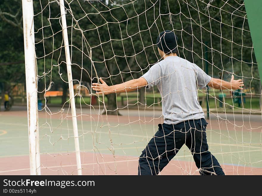 A man, standing with his arms wide open, in front of the goalie net, acting to be a soccer goalie. - horizontally framed. A man, standing with his arms wide open, in front of the goalie net, acting to be a soccer goalie. - horizontally framed