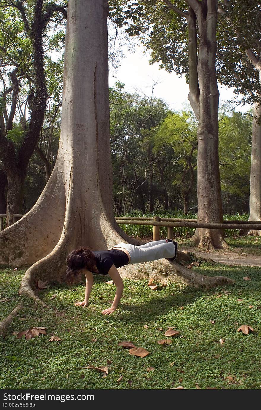 Young, attractive woman is performing a push-up next to a tree. Vertically framed shot. Young, attractive woman is performing a push-up next to a tree. Vertically framed shot