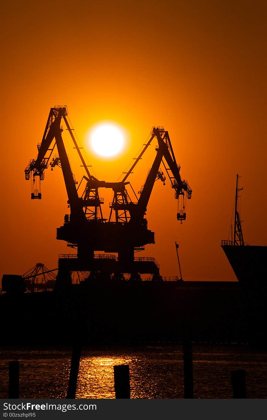 A pair of cargo cranes sit at rest in a industrial shipyard at sunset. A pair of cargo cranes sit at rest in a industrial shipyard at sunset