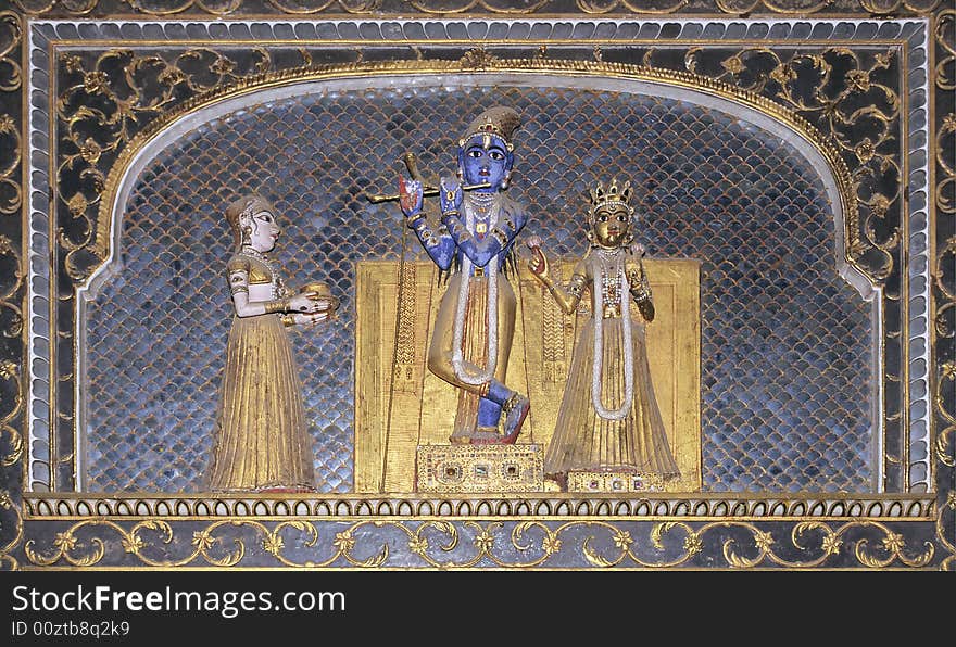 Colored statues encrusted with gems of hindu god Vishnu playing flute with goddesses on blue ceramics background in the maharajah palace of bikaner, Rajasthan, India. Colored statues encrusted with gems of hindu god Vishnu playing flute with goddesses on blue ceramics background in the maharajah palace of bikaner, Rajasthan, India.