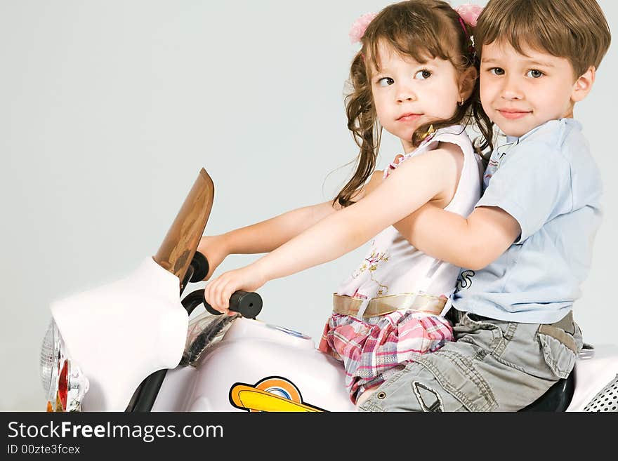 Adorable boy and little girl sitting on white toy bike