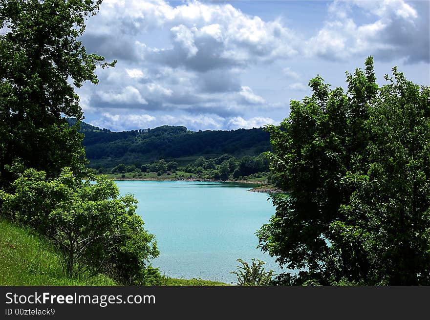 A view of mountain landscape with a small lake and rainy sky. A view of mountain landscape with a small lake and rainy sky