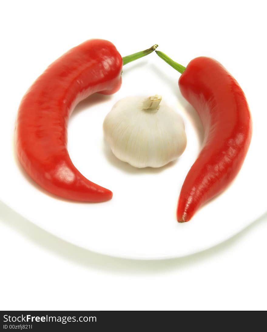 Two fresh chili peppers and a bulb of garlic on a white plate and isolated on white background. Two fresh chili peppers and a bulb of garlic on a white plate and isolated on white background