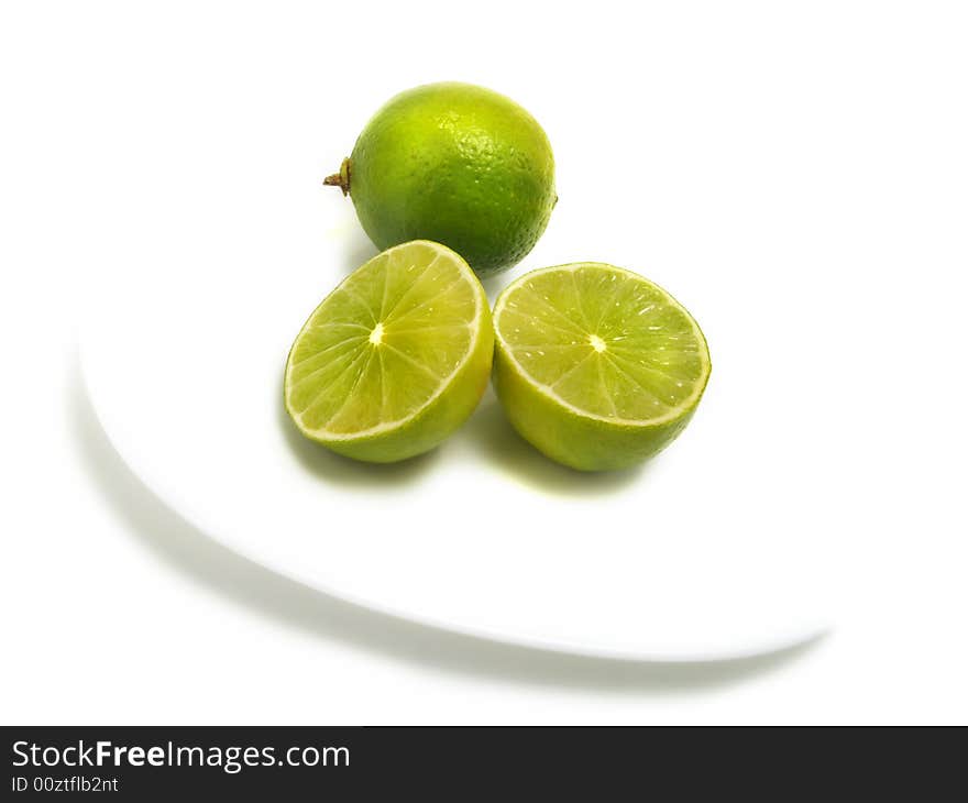 A group of half and whole fresh limes on white plate and isolated on white background. A group of half and whole fresh limes on white plate and isolated on white background