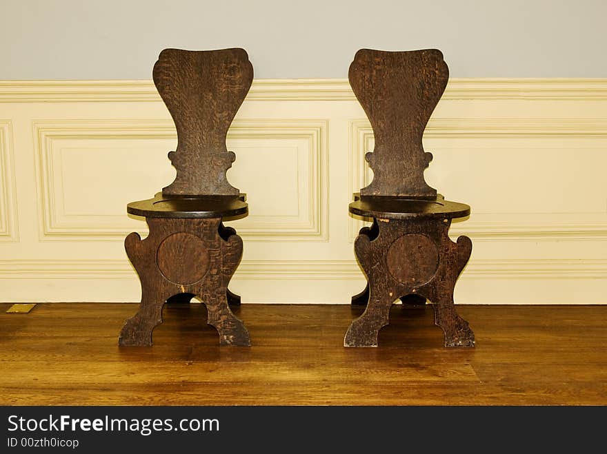 A pair of antique oak chairs in a part panelled classic interior