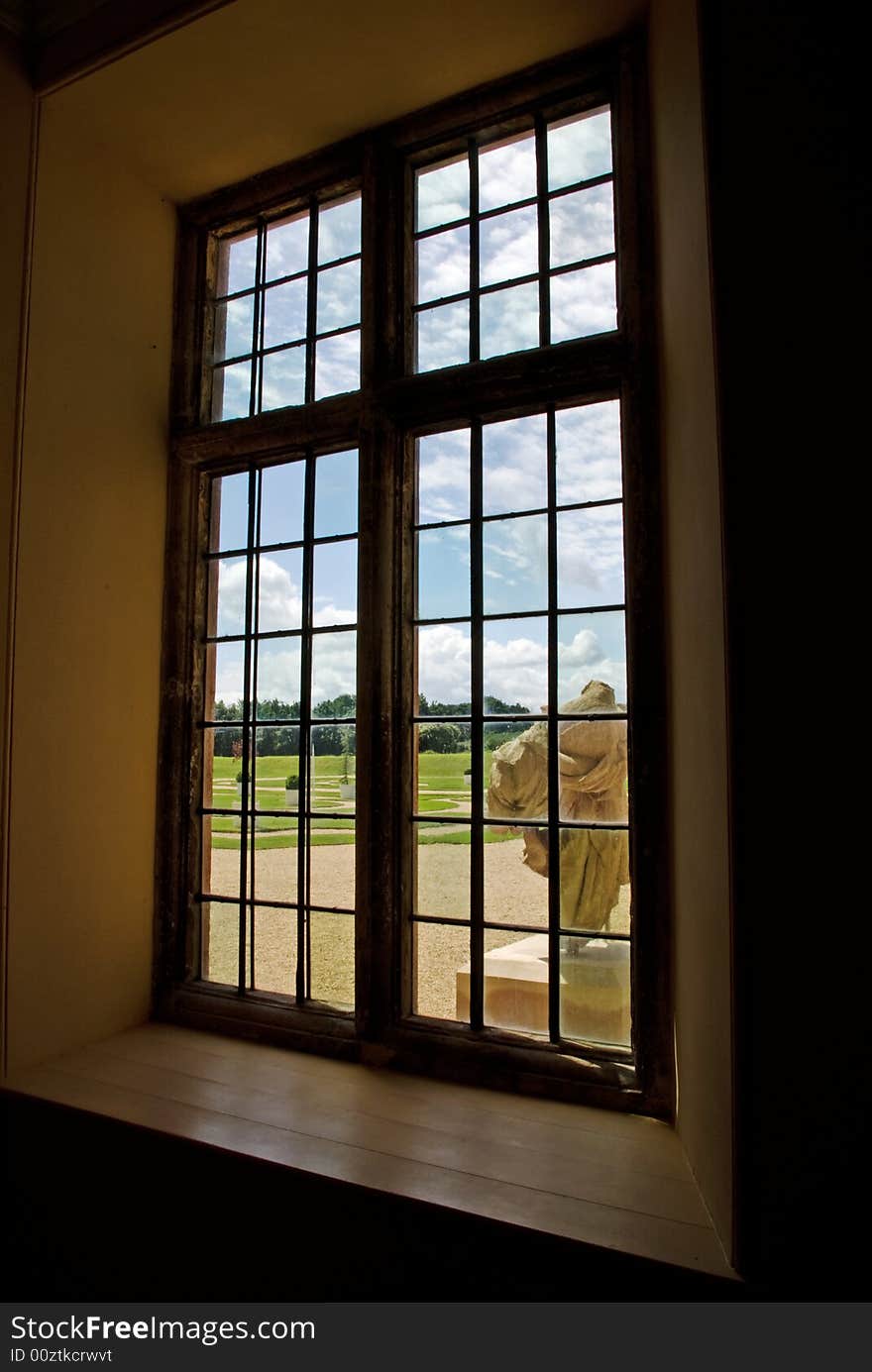 A sunny outlook from a stone mullioned window onto a bright and expansive fromal garden. A sunny outlook from a stone mullioned window onto a bright and expansive fromal garden