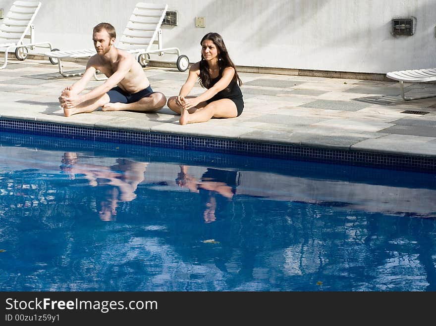 A couple stretching their legs by the poolside, smiling and concentrating - horizontally framed. A couple stretching their legs by the poolside, smiling and concentrating - horizontally framed