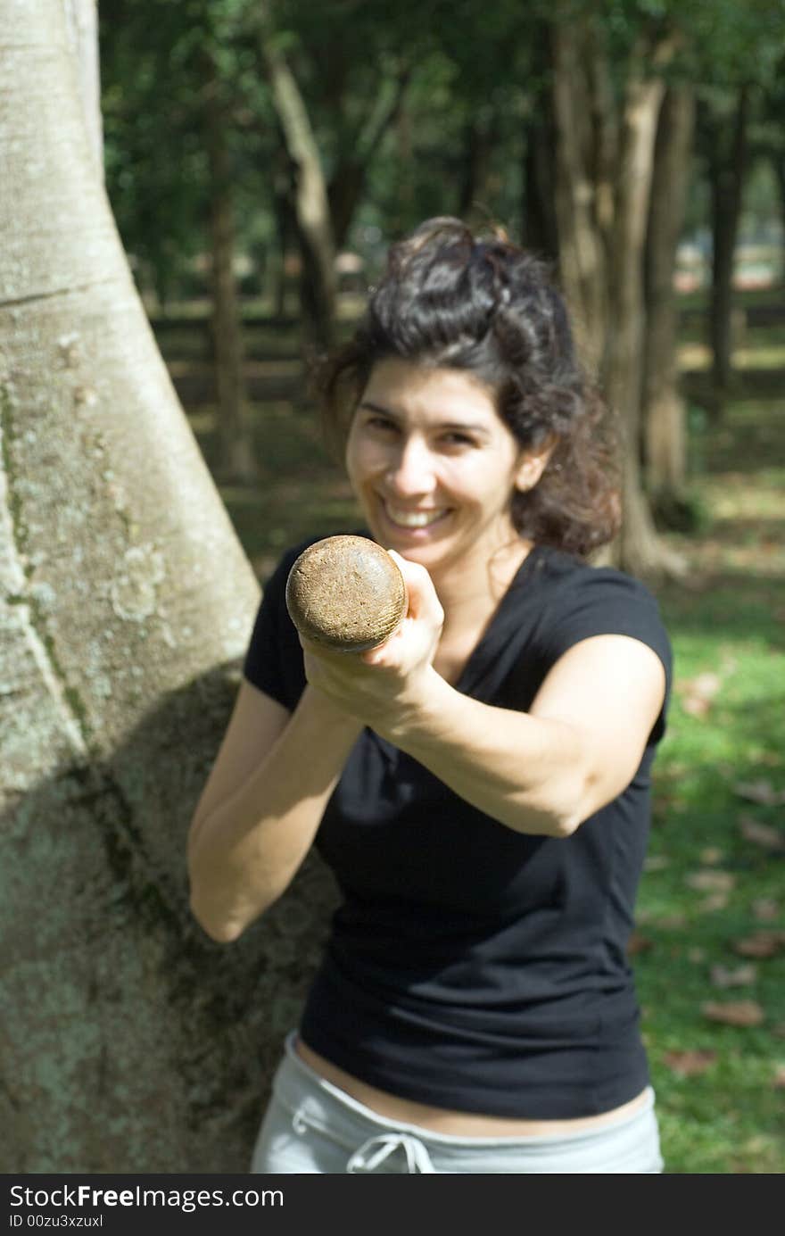 A young, attractive woman is standing next to a tree in a park. She is looking at the camera and jokingly holding a baseball bat to the camera. Vertically framed photo. A young, attractive woman is standing next to a tree in a park. She is looking at the camera and jokingly holding a baseball bat to the camera. Vertically framed photo.