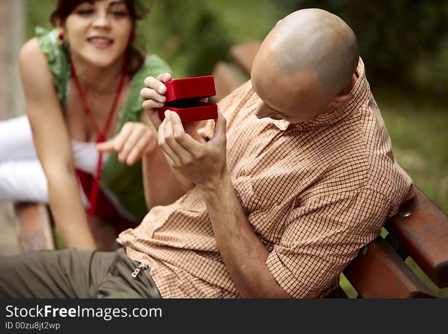 Playful man opening slowly a red ring box making a young lady to be very curios what's inside. Playful man opening slowly a red ring box making a young lady to be very curios what's inside