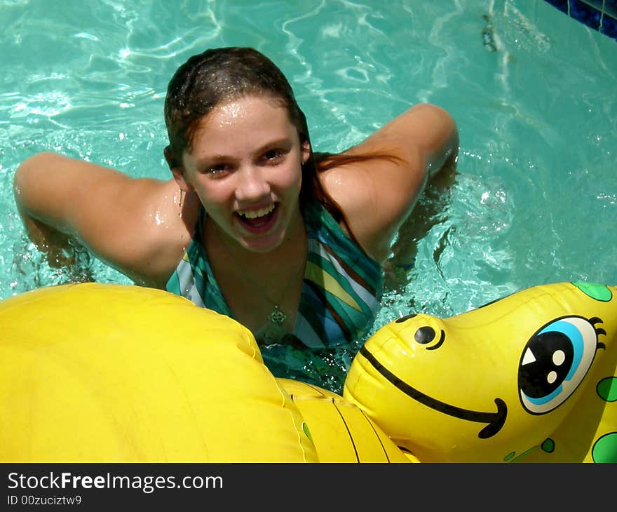 A picture of a cute girl smiling in the swimming pool with a dragon floaty toy. A picture of a cute girl smiling in the swimming pool with a dragon floaty toy.