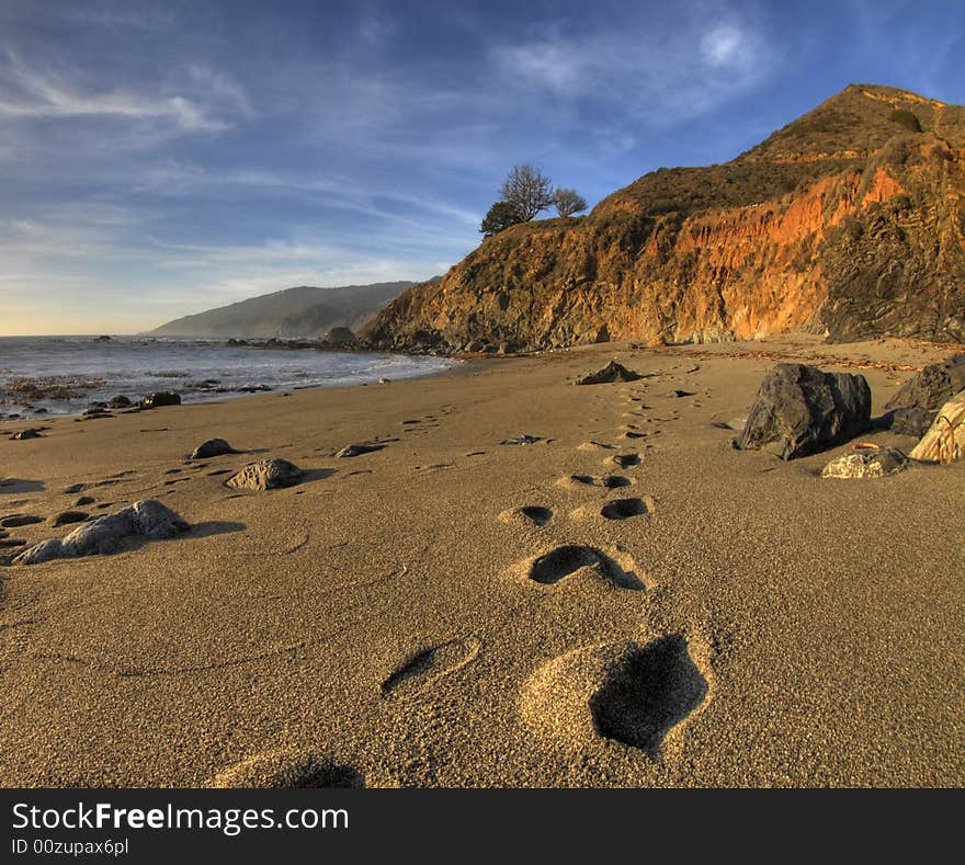 Footprints going into the distance on the beach with the water, cliffs and beautiful sky in thebackground. Footprints going into the distance on the beach with the water, cliffs and beautiful sky in thebackground