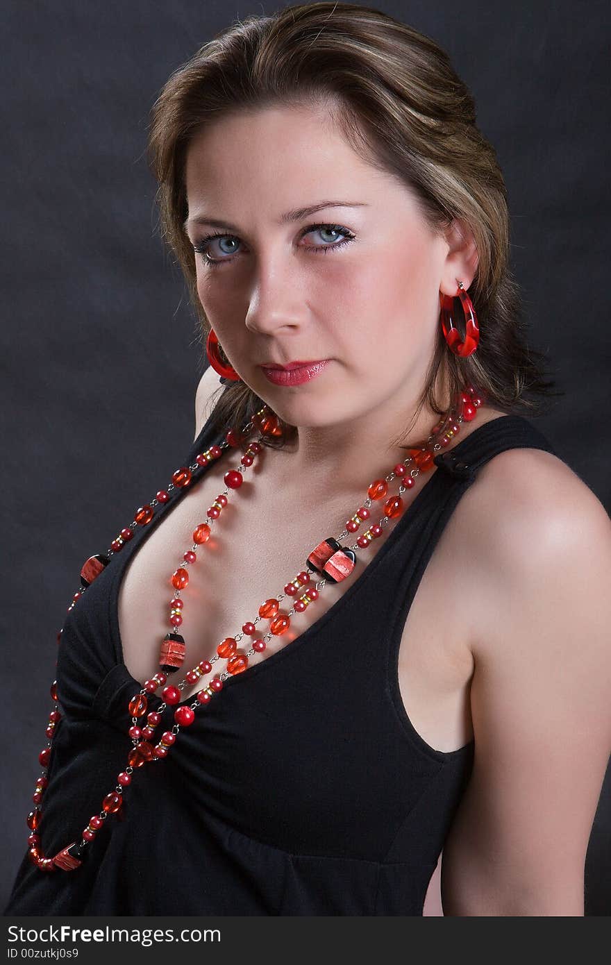 Portrait of the beautiful young girl in a red beads on a dark background. Portrait of the beautiful young girl in a red beads on a dark background