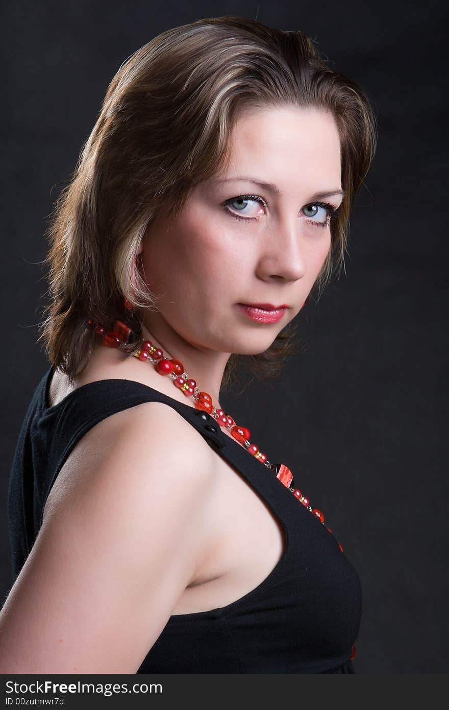 Portrait of the beautiful young girl in a red beads on a dark background. Portrait of the beautiful young girl in a red beads on a dark background