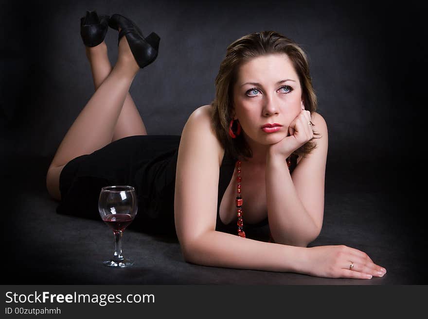 Nice girl with a glass of red wine lay on a dark background. Nice girl with a glass of red wine lay on a dark background