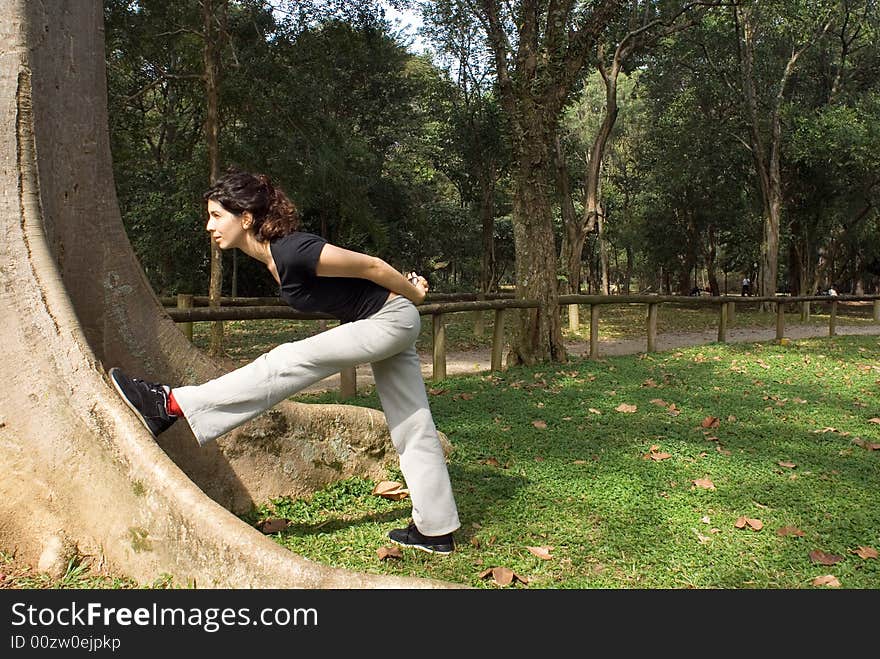 A young, attractive woman is standing next to a tree. She is looking at the tree, leaning against it and stretching. Horizontally framed photo. A young, attractive woman is standing next to a tree. She is looking at the tree, leaning against it and stretching. Horizontally framed photo.