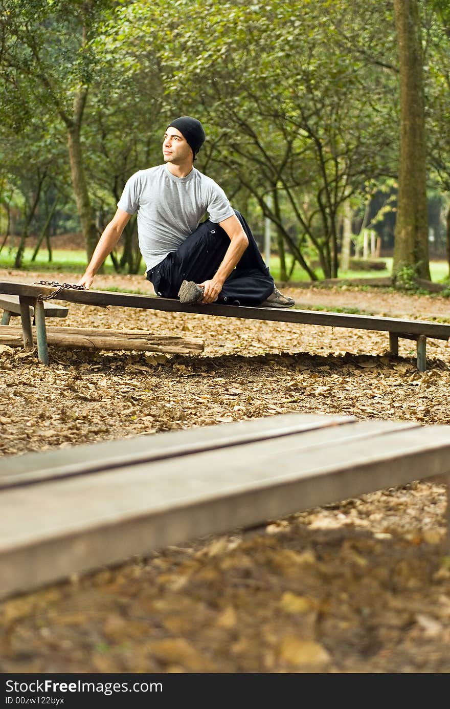 A male, sitting on a park bench, stretching - vertically framed. A male, sitting on a park bench, stretching - vertically framed