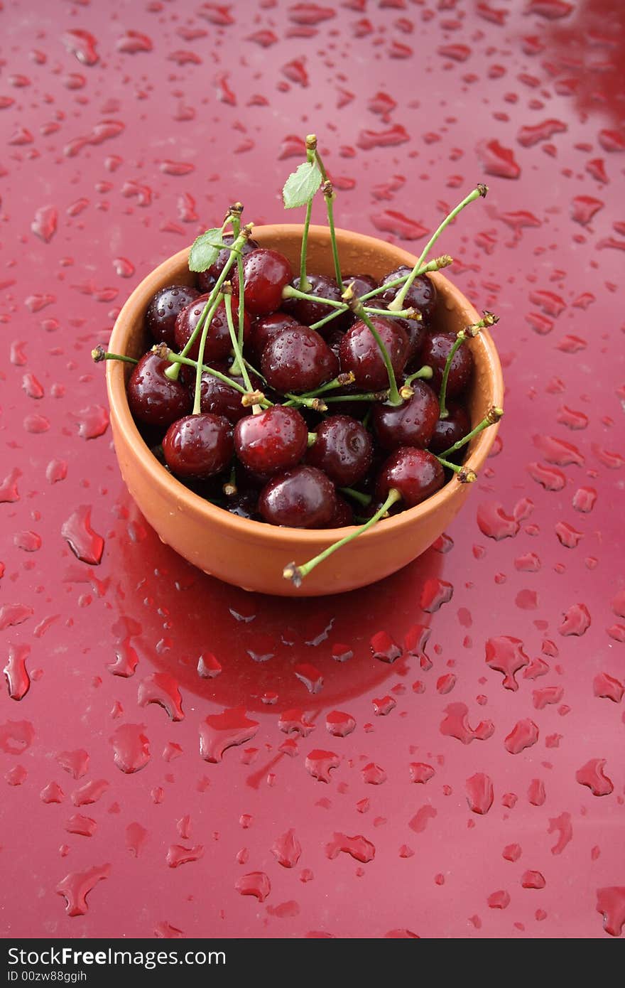 Cherries, with drops of water, in a brown ceramic cup on a red background