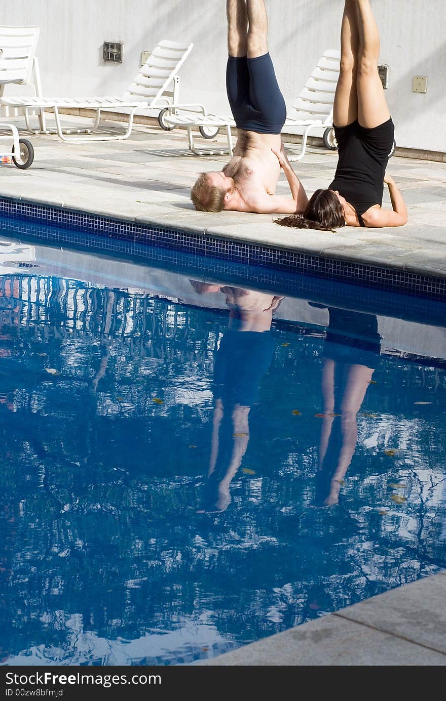 A couple, by the pool, stretch with each other, doing candlestick - vertically framed. A couple, by the pool, stretch with each other, doing candlestick - vertically framed