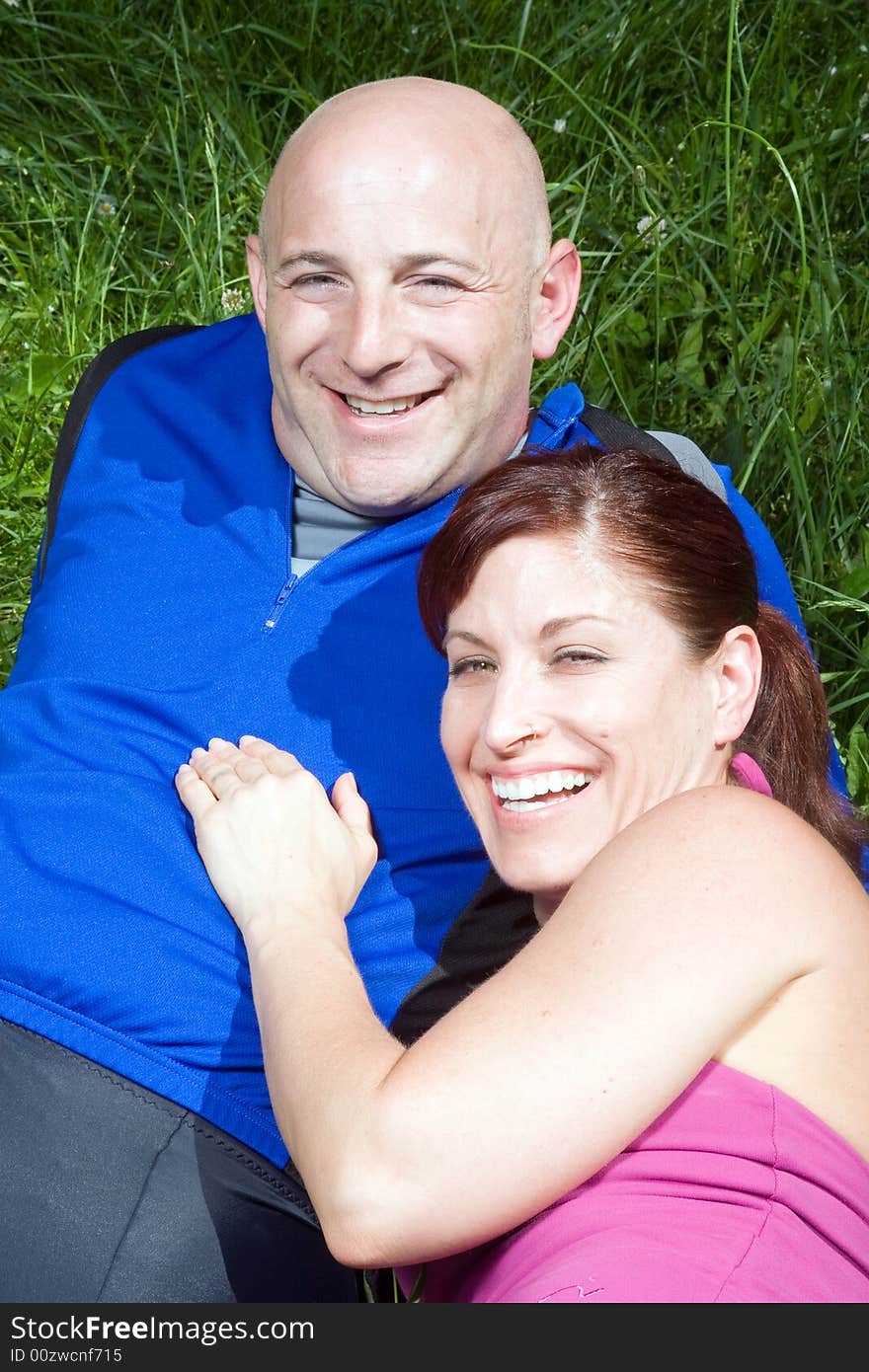 Happy couple sitting on the grass laughing. Vertically framed photograph. Happy couple sitting on the grass laughing. Vertically framed photograph