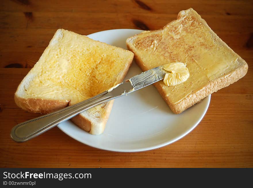 Two pieces of bread with butter and a knife in a wooden table. Two pieces of bread with butter and a knife in a wooden table