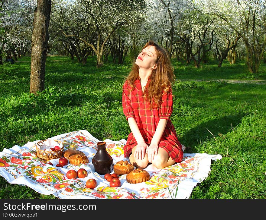 The young red-haired woman is having a picnic in the spring garden. The young red-haired woman is having a picnic in the spring garden