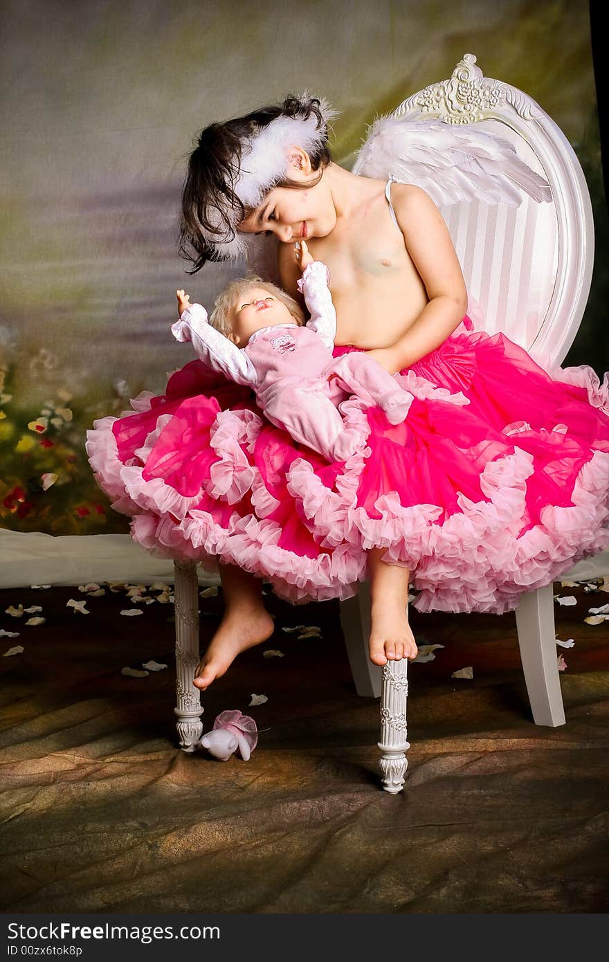 Cute girl wearing angel wings and a pettiskirt is playing with her baby doll. Cute girl wearing angel wings and a pettiskirt is playing with her baby doll