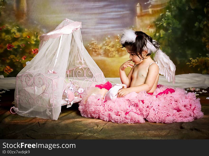 Cute girl wearing angel wings and a pettiskirt is playing with her baby doll. Cute girl wearing angel wings and a pettiskirt is playing with her baby doll