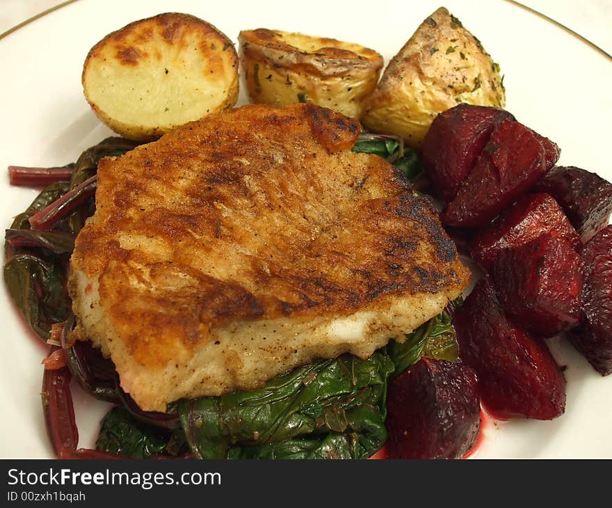 Photo of fillet of pan seared Tautog or Black Fish served with roasted beets, roasted potatoes and served on a bed of beet greens.  The Tautog or Black Fish can be substituted for any white meat fish and is quite good.