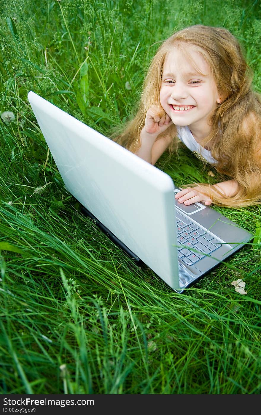 Cute little girl with laptop in green grass